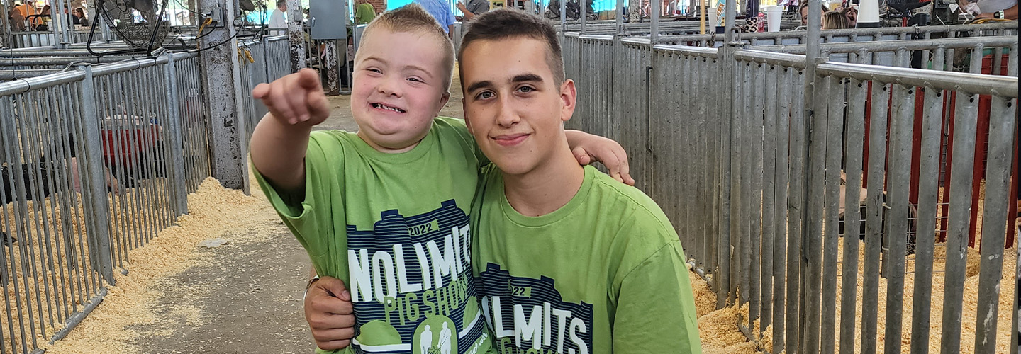 A teen boy and younger boy posing for the camera in the swine barn on the fairgrounds