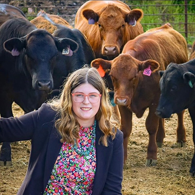 Riglee Welty posing in a field in front of several cows