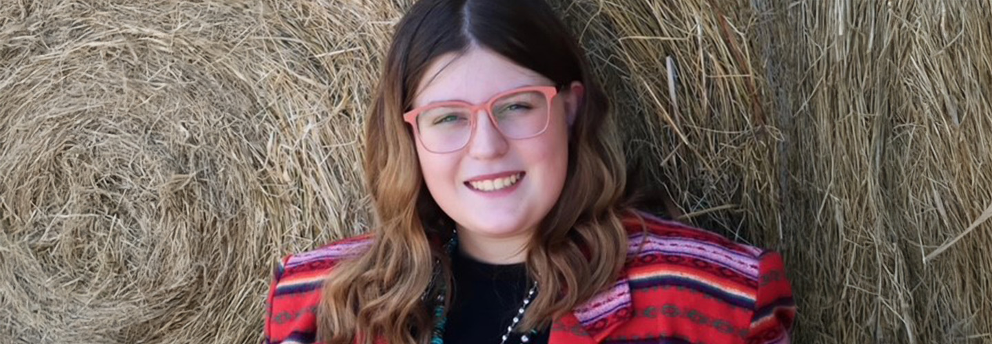 A girl sitting in front of a hay bale